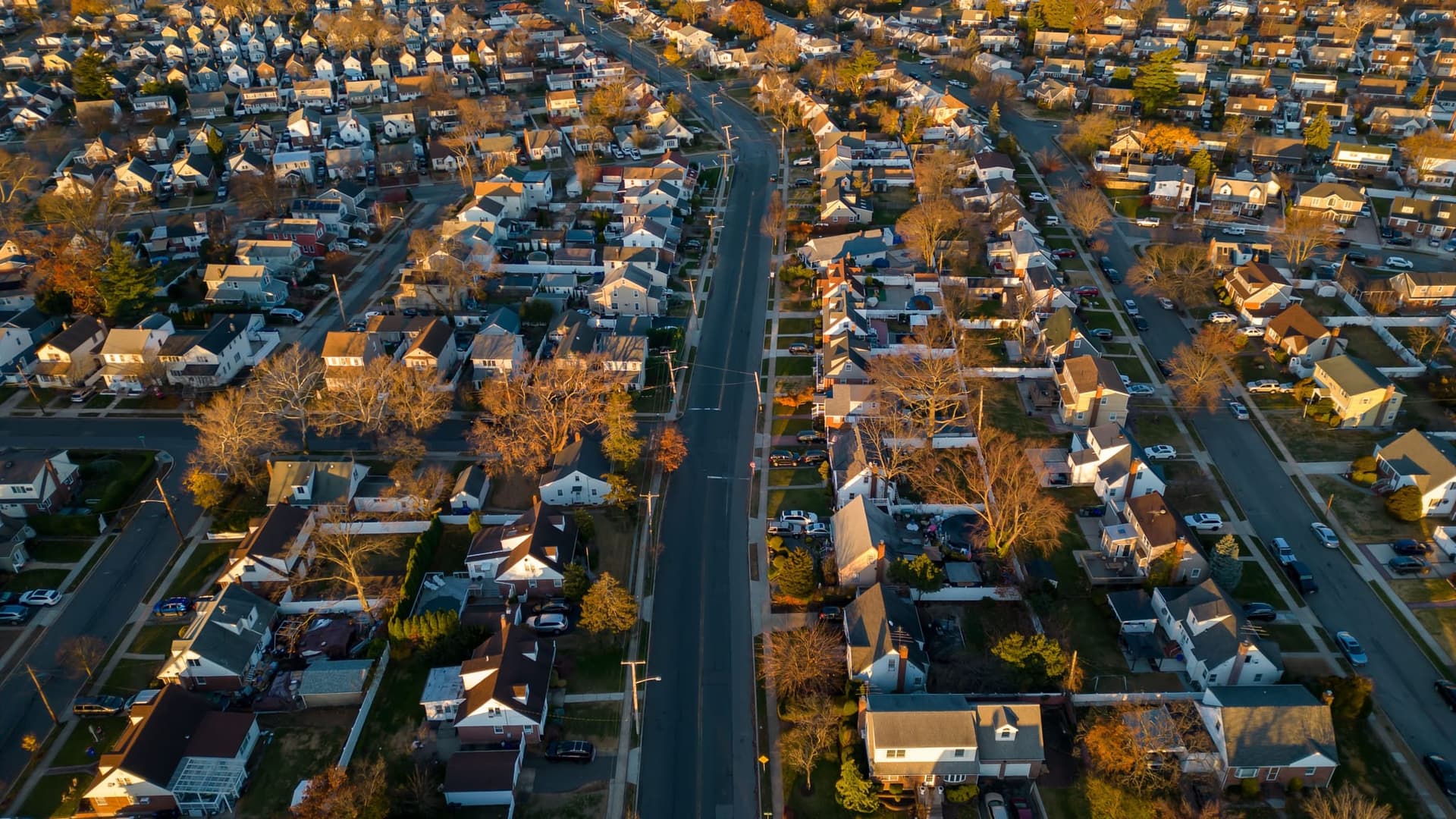 Aerial view of a dense suburban neighborhood of rooftops among autumn trees