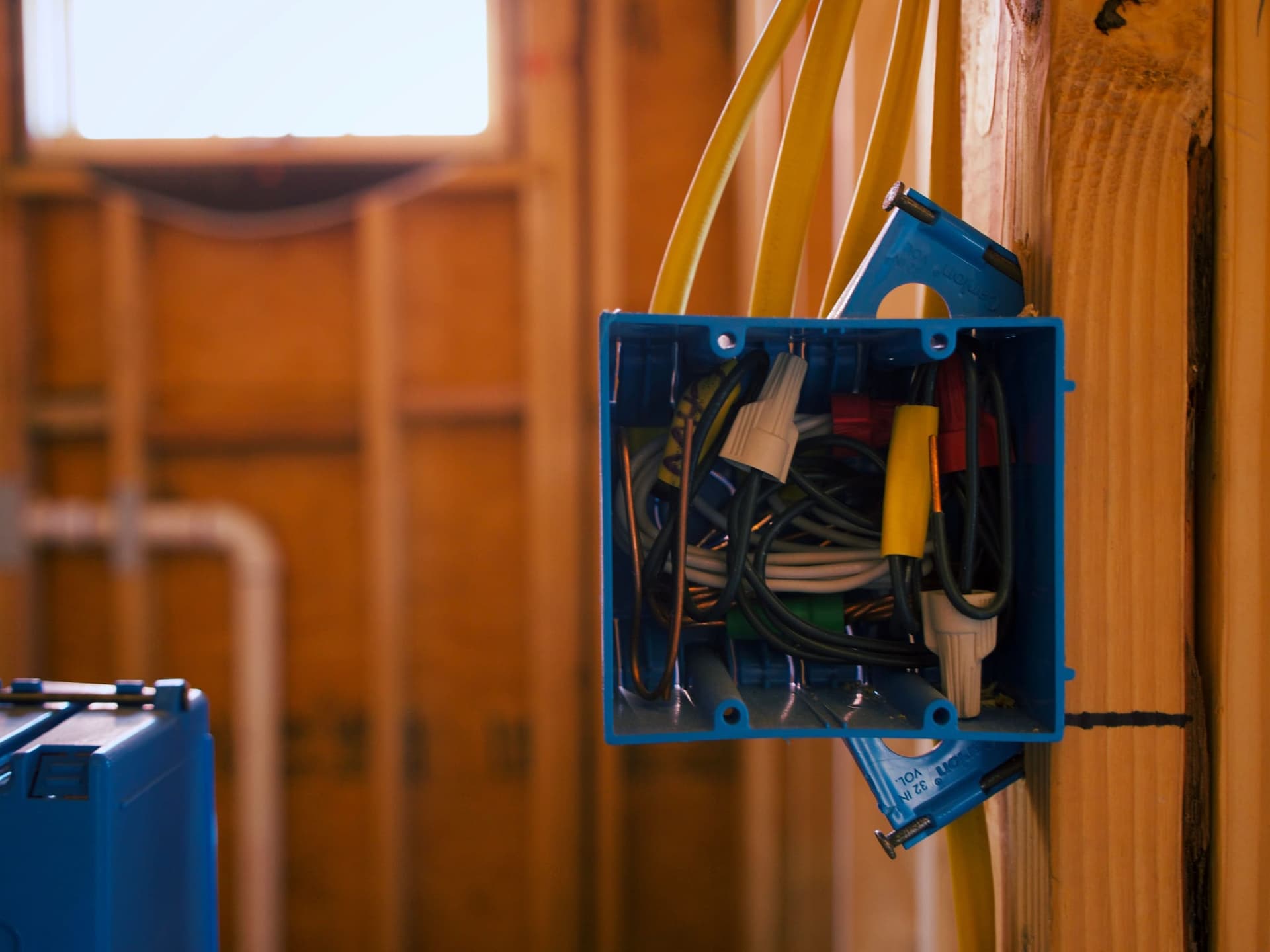 An open blue electrical junction box mounted to a wall stud, packed with wiring