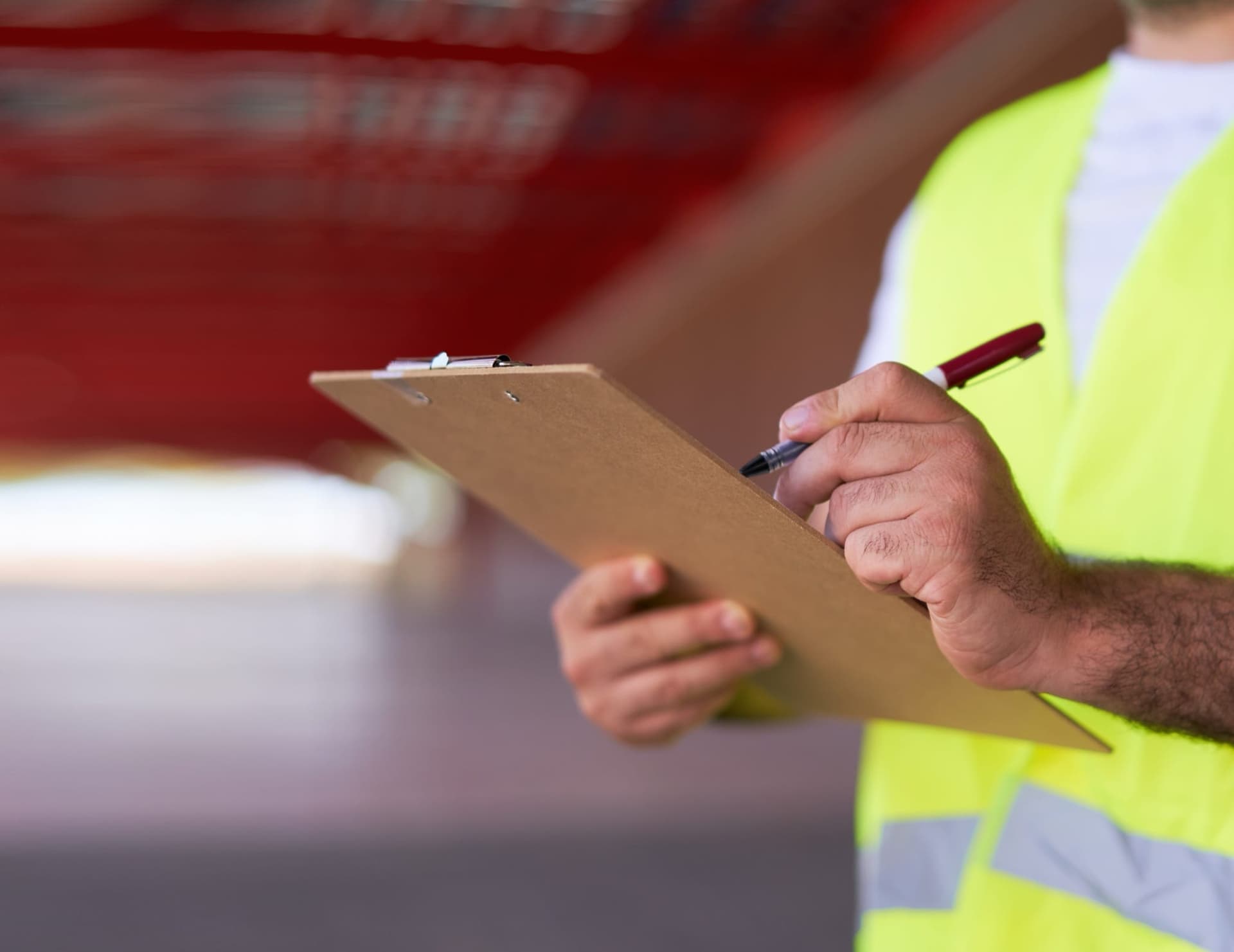Close-up of an inspector in a hi-vis vest writing on a clipboard
