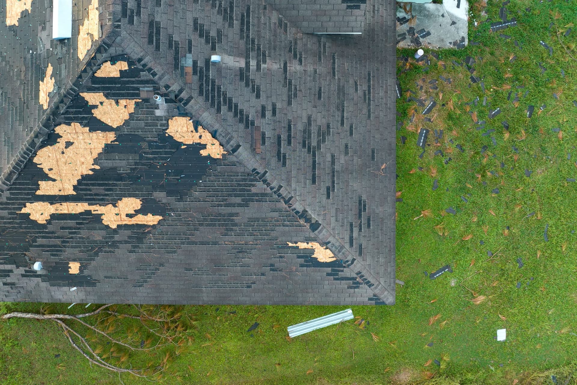 Overhead view of a storm-damaged shingle roof, with shingles torn away exposing bare decking underneath