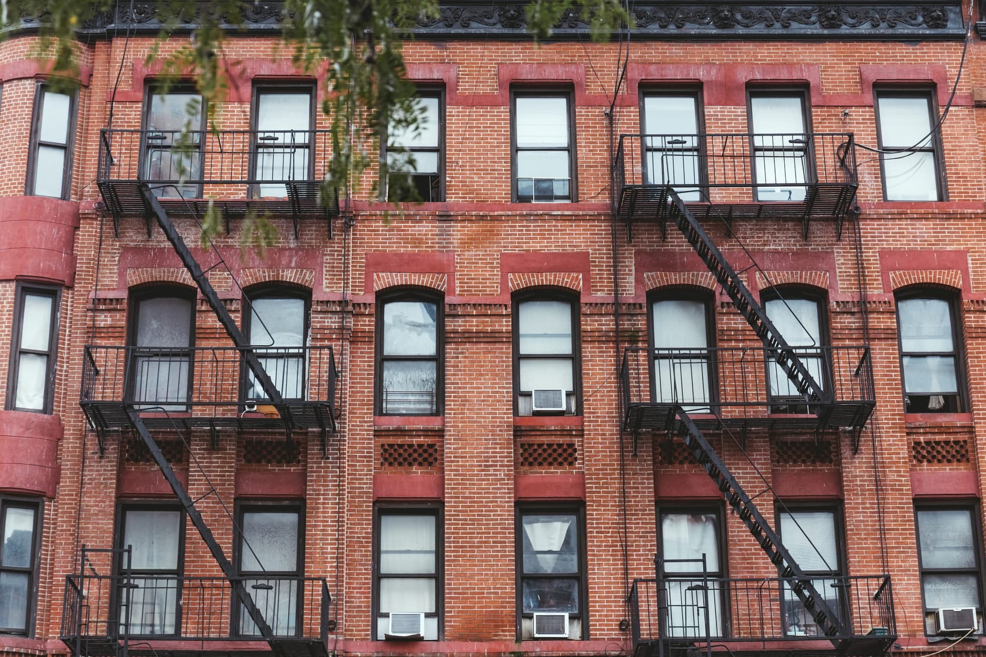 The facade of an older red-brick apartment building fronted by black iron fire escapes