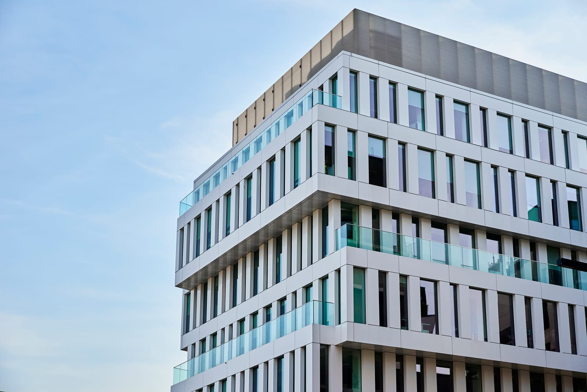 The facade of a modern white and glass mid-rise office building against a blue sky