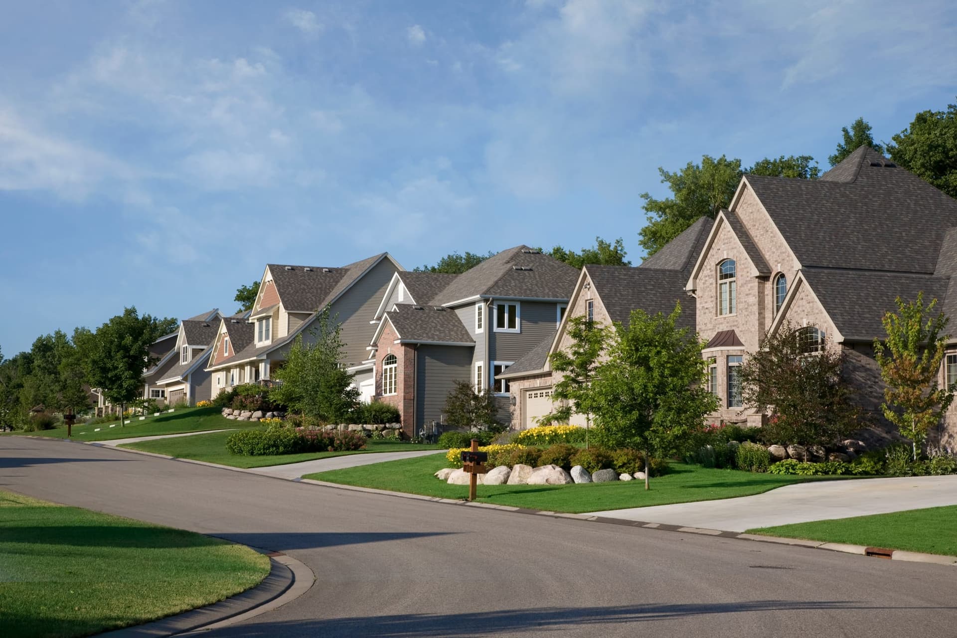 A street of large two-story homes with manicured front lawns on a clear summer day
