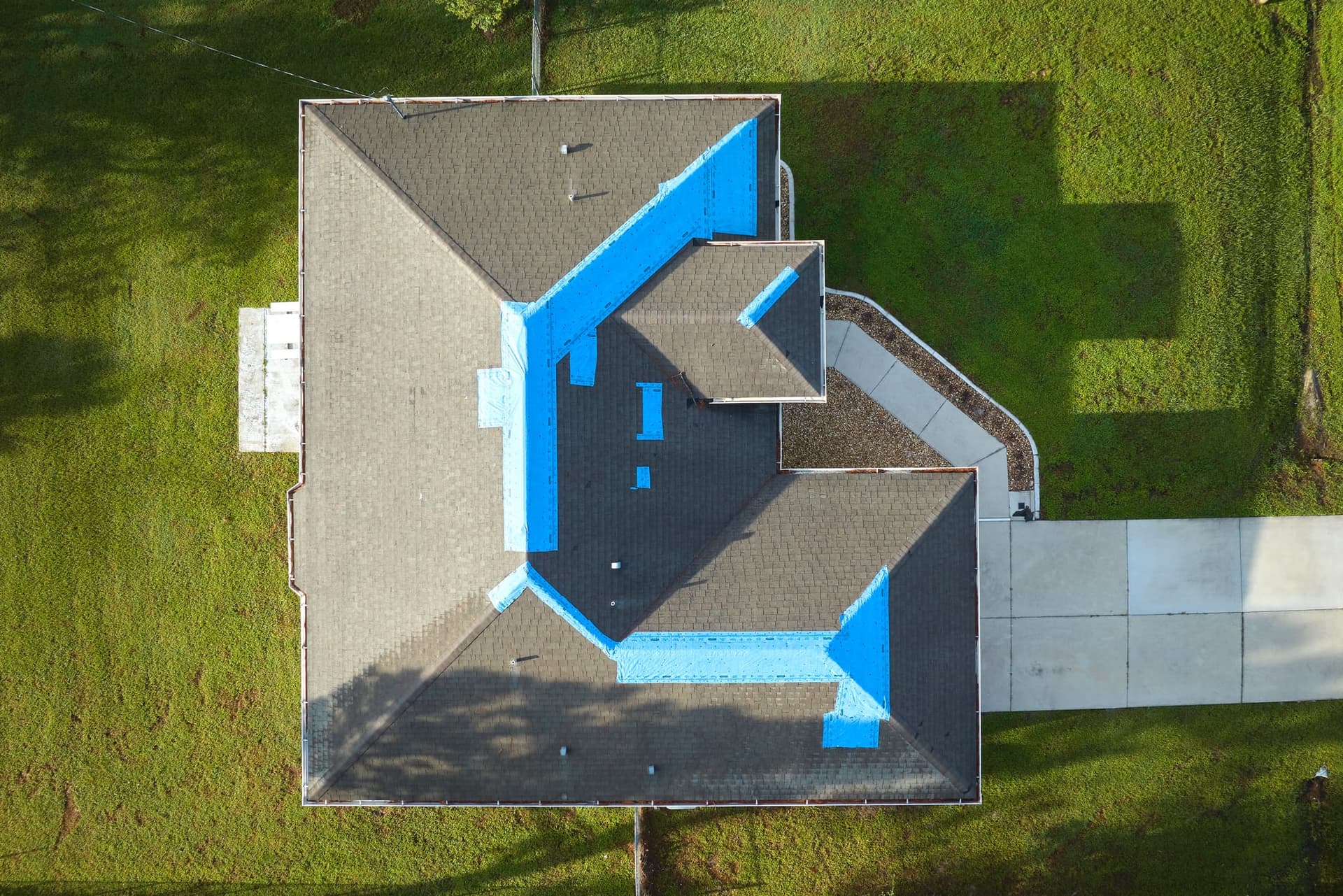 Aerial view of a house roof with large sections covered by a blue protective tarp